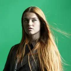 Mujer pelirroja con pecas, su cabello largo y suelto se mueve con el viento. La edición de **dodge and burn** resalta sus rasgos.