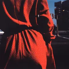 Un vestido rojo con pequeños triángulos blancos, capturado por harry callahan photography, se funde con las sombras de una calle urbana.