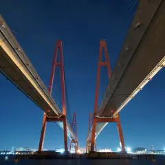 Dos torres rojas de un puente atirantado crean un efecto de fotos simétricas contra el cielo nocturno azul.