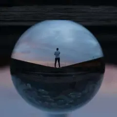 Un hombre mira el atardecer a través de una esfera de cristal, creando fotos originales y creativas.