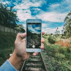 Mano sujeta móvil para capturar vía de tren. ¡Descubre trucos para hacer fotos originales y únicas!