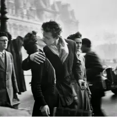 Pareja besándose apasionadamente en París, rodeada de gente y un coche antiguo. Un momento capturado en estas fotos históricas.