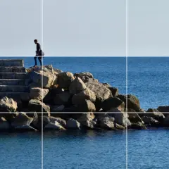 Un hombre camina por unas escaleras de piedra hacia el mar, siguiendo la regla de los tercios vertical.