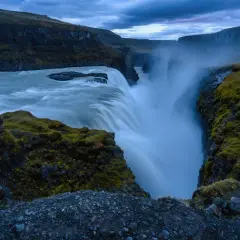 Cascada imponente con agua que cae en un cañón, creando un **efecto seda** bajo un cielo nublado.