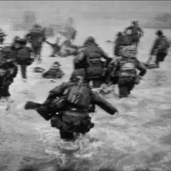 Soldados avanzan en el agua durante el desembarco de Normandía, una escena icónica capturada por Robert Capa.