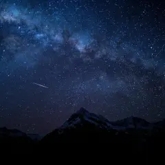Una estrella fugaz cruza el cielo nocturno estrellado, con la Vía Láctea visible sobre montañas nevadas. Fotos perseidas capturan la magia.