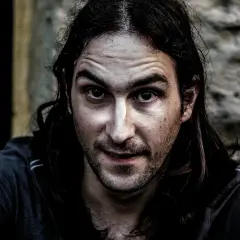 Primer plano de un hombre con cabello largo y oscuro, mirada intensa y piel con un efecto dragan photoshop que acentúa las texturas.