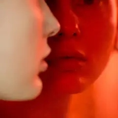 Primer plano de dos rostros, uno iluminado en rojo intenso, el otro en tonos claros. Martina Matencio captura un momento íntimo y enigmático.