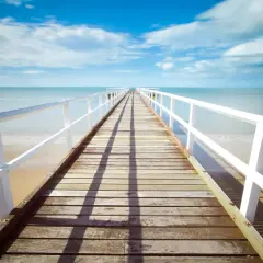 Un muelle de madera se extiende hacia el mar azul bajo un cielo nublado. La foto perspectiva crea una sensación de profundidad y calma.