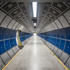 Pasillo circular de metro con paneles azules y grises, y líneas convergentes que crean una perspectiva infinita.