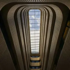 Interior de un edificio con un tragaluz rectangular. Las paredes curvas y las barandillas crean un efecto de túnel, jugando con formas geométricas básicas.