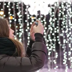 Chica con bufanda oscura toma foto de luces navideñas con un hermoso efecto bokeh.