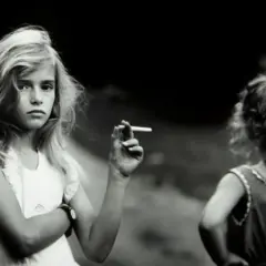Una niña rubia, en una de las sally mann fotos, sostiene un cigarrillo. Otra niña, de espaldas, mira hacia la derecha.