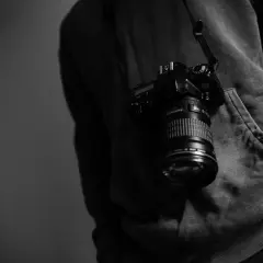 Cámara colgada del cuello de un sudadera, lista para capturar momentos como los de los fotógrafos famosos actuales.