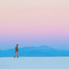 Hombre camina sobre dunas blancas bajo un cielo degradado de rosa y azul, respetando la ley del horizonte.