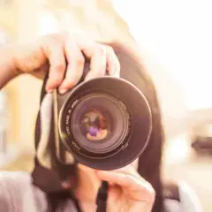 Manos sostienen una cámara Canon, capturando un momento para su proyecto fotográfico. El sol brilla intensamente.