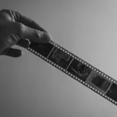 Mano sostiene tira de película en blanco y negro, lista para rebelar foto. Se aprecian imágenes de coches antiguos.