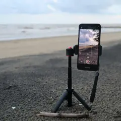 Un tripode casero sostiene un teléfono móvil en la playa, listo para grabar el mar y el cielo.