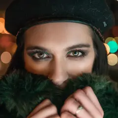 Ojos penetrantes de mujer con boina negra y abrigo de pelo verde, rodeada de luces bokeh. Un reto fotográfico nocturno.