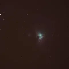 Nebulosa verdosa en el cielo nocturno, rodeada de estrellas y con tenues estelas de estrellas.