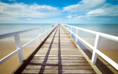 Un muelle de madera se extiende hacia el mar azul bajo un cielo nublado. La foto perspectiva crea una sensación de profundidad y calma.