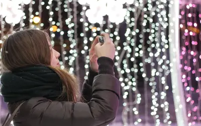 Chica con bufanda oscura toma foto de luces navideñas con un hermoso efecto bokeh.