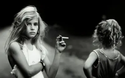 Una niña rubia, en una de las sally mann fotos, sostiene un cigarrillo. Otra niña, de espaldas, mira hacia la derecha.
