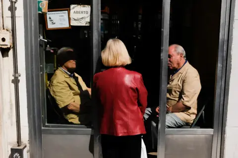 Una mujer de rojo observa a dos hombres dentro de una barbería. La composición sigue la regla de los tercios, creando una escena intrigante.