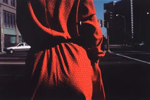 Un vestido rojo con pequeños triángulos blancos, capturado por harry callahan photography, se funde con las sombras de una calle urbana.