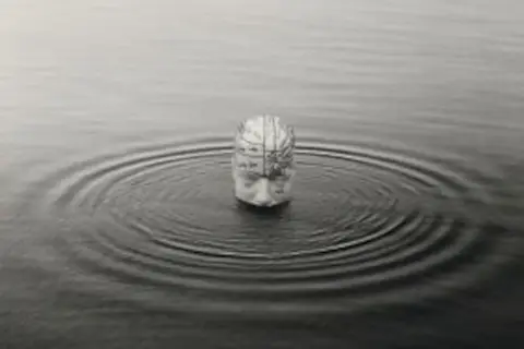 Una cabeza humana con un mapa cerebral emerge del agua, creando ondas concéntricas. Una de las icónicas chema madoz fotos.