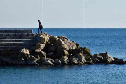 Un hombre camina por unas escaleras de piedra hacia el mar, siguiendo la regla de los tercios vertical.