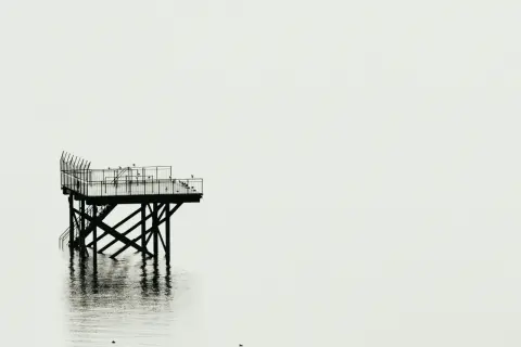 Plataforma solitaria sobre el agua, reflejo nítido. Fotografía minimalista que evoca calma y soledad.