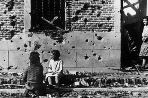 Niños juegan entre escombros frente a un edificio bombardeado, una escena conmovedora capturada en una de las robert capa fotos famosas.