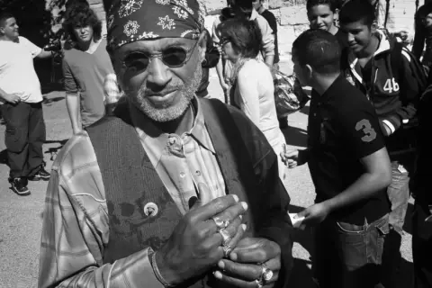 Stanley Greene, con su bandana y anillos, sonríe rodeado de jóvenes.