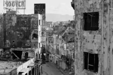 Calle devastada con edificios en ruinas, un cartel de "HOOVER" en lo alto. La mirada de Gabriele Basilico captura la desolación.