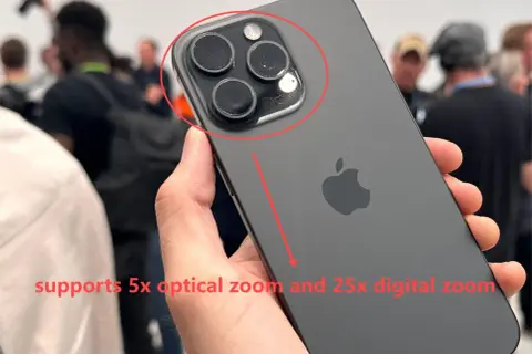 Mano sostiene un iPhone oscuro, mostrando su sistema de cámaras. El texto indica "zoom digital" de 25x y zoom óptico de 5x.