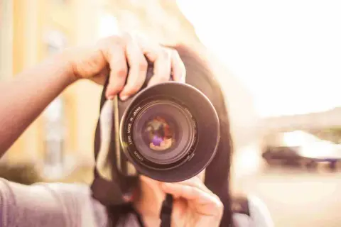 Manos sostienen una cámara Canon, capturando un momento para su proyecto fotográfico. El sol brilla intensamente.