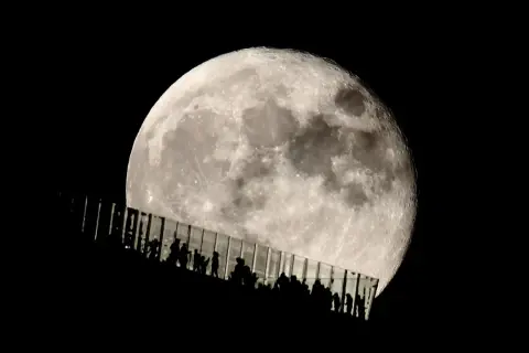 Siluetas de personas observan la luna llena desde una pasarela de cristal. Los parámetros de la foto de la luna capturan su textura y brillo.