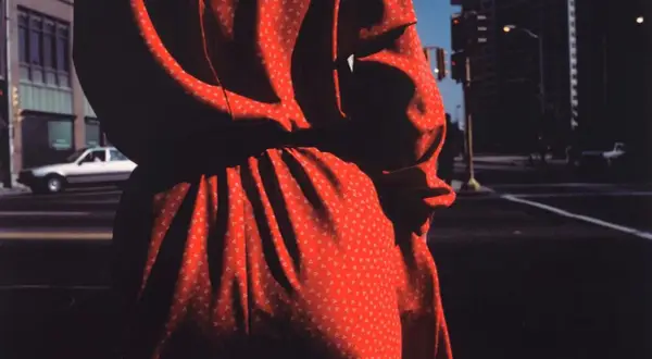 Un vestido rojo con pequeños triángulos blancos, capturado por harry callahan photography, se funde con las sombras de una calle urbana.