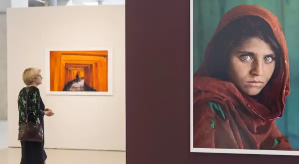 Una mujer observa una obra de Steve McCurry, destacando la icónica mirada de la niña afgana.
