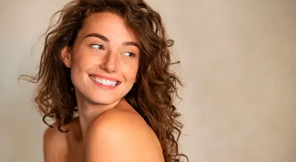 Mujer sonriente con pecas, cabello rizado y mirada radiante. Sigue la regla de la mirada para capturar su belleza natural.