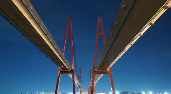 Dos torres rojas de un puente atirantado crean un efecto de fotos simétricas contra el cielo nocturno azul.