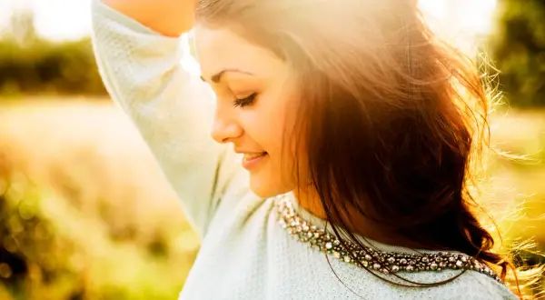 Momentos capturados en estas fotos pilladas: una joven sonríe con el sol en su rostro, su cabello suelto y un suéter adornado.