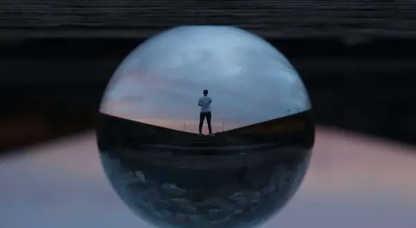 Un hombre mira el atardecer a través de una esfera de cristal, creando fotos originales y creativas.