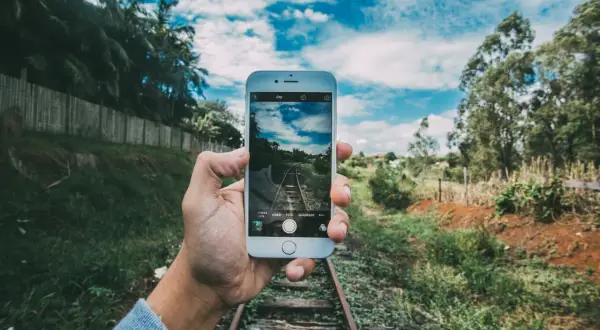 Mano sujeta móvil para capturar vía de tren. ¡Descubre trucos para hacer fotos originales y únicas!