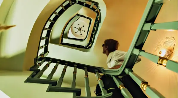 Vista en plano nadir de una escalera de caracol con una mujer mirando hacia arriba.