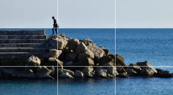 Un hombre camina por unas escaleras de piedra hacia el mar, siguiendo la regla de los tercios vertical.