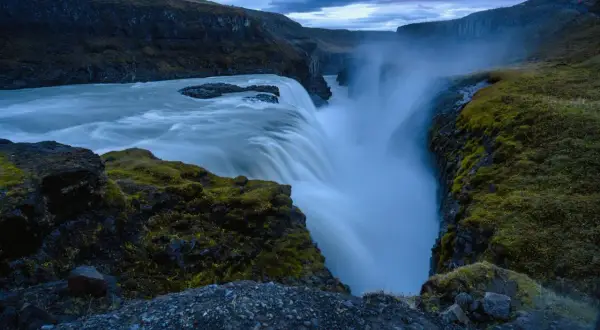 Cascada imponente con agua que cae en un cañón, creando un **efecto seda** bajo un cielo nublado.