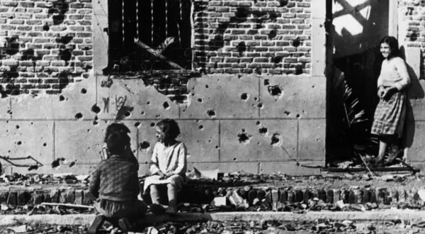 Niños juegan entre escombros frente a un edificio bombardeado, una escena conmovedora capturada en una de las robert capa fotos famosas.
