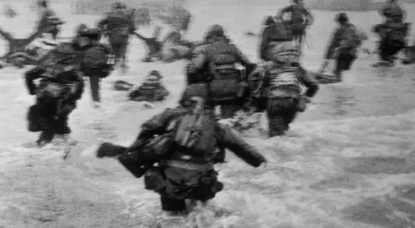 Soldados avanzan en el agua durante el desembarco de Normandía, una escena icónica capturada por Robert Capa.